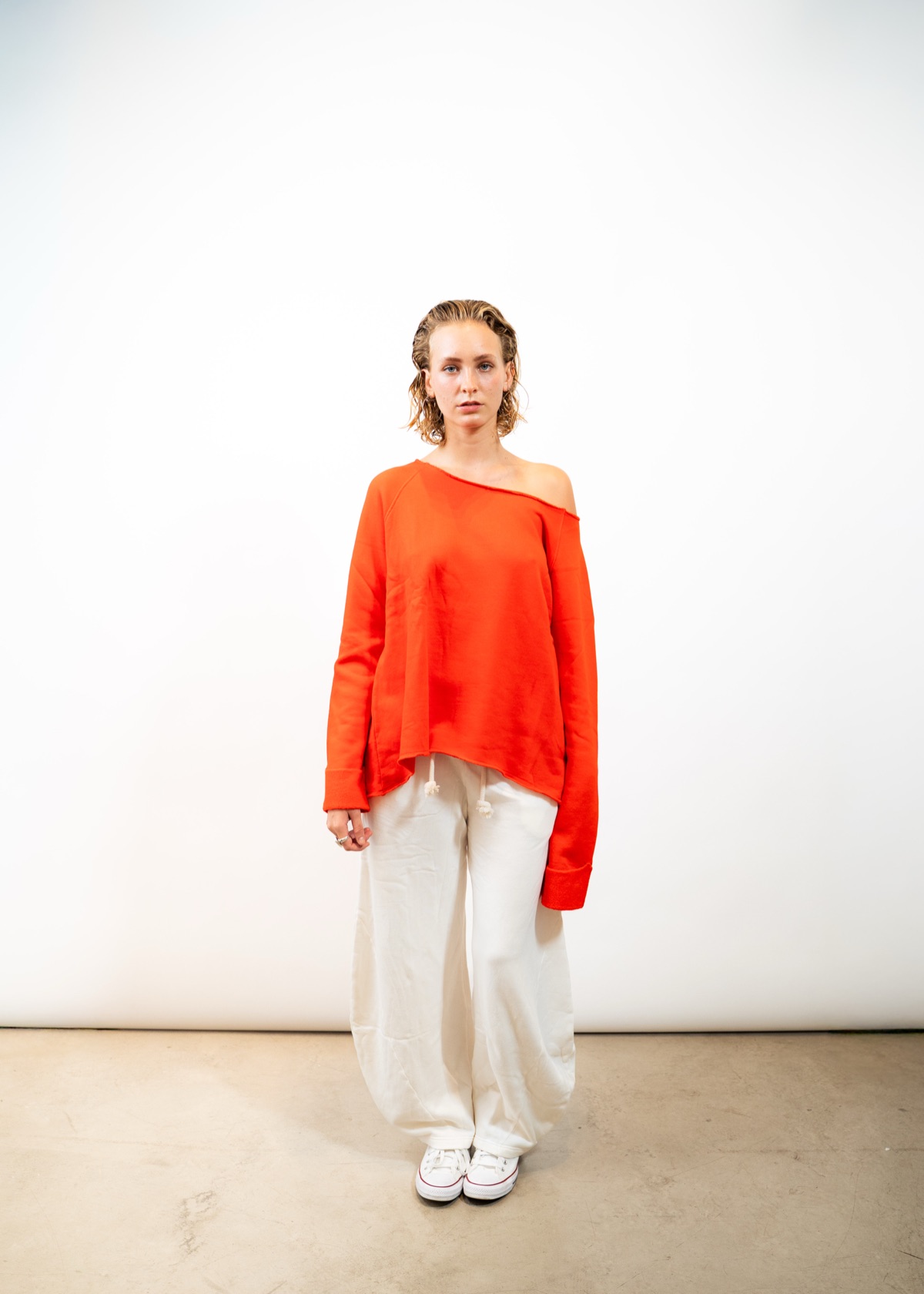 Outryght Wintershoot: Model in oranger Strickjacke und heller Hose vor weißem Studiohintergrund